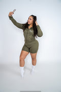 Model taking a mirror selfie in the NoLuxx Olive Green Sculpt Set with a zip-front jacket and biker shorts.