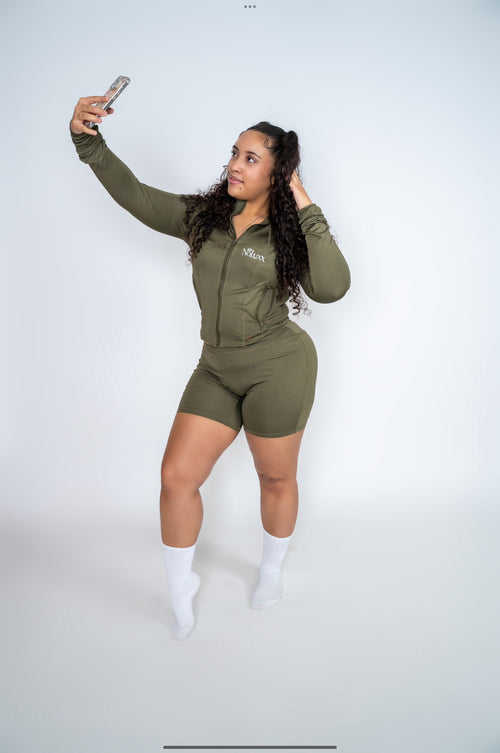 Model taking a mirror selfie in the NoLuxx Olive Green Sculpt Set with a zip-front jacket and biker shorts.