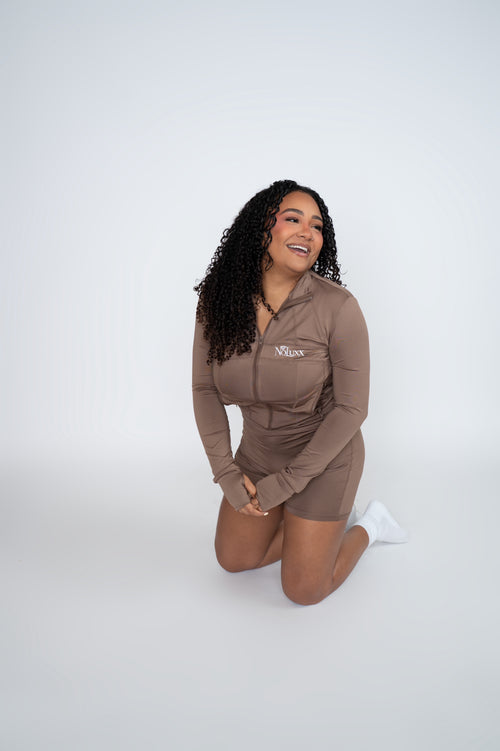 Model kneeling in the NoLuxx Brown Sculpt Set with a zip-front jacket and biker shorts.